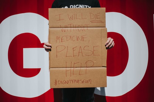 Cardboard sign that says "I will DIE without medicine, please help #DignityMuseum"