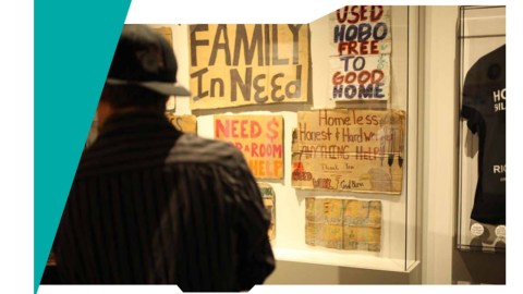 A man stands facing a wall with various handwritten signs from people who have experienced homelessness.