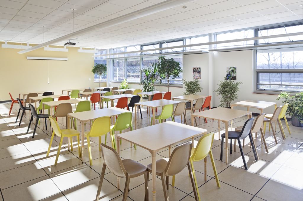 A naturally lit room with tables surrounded by chairs of different colors, including bright yellows and greens.