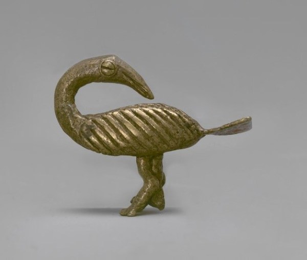 A small brass sculpture of a stylized bird with its neck turned around to face its tail feather.