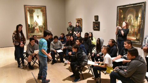 A young visitor stands in front of a larger group of visitors in a gallery.