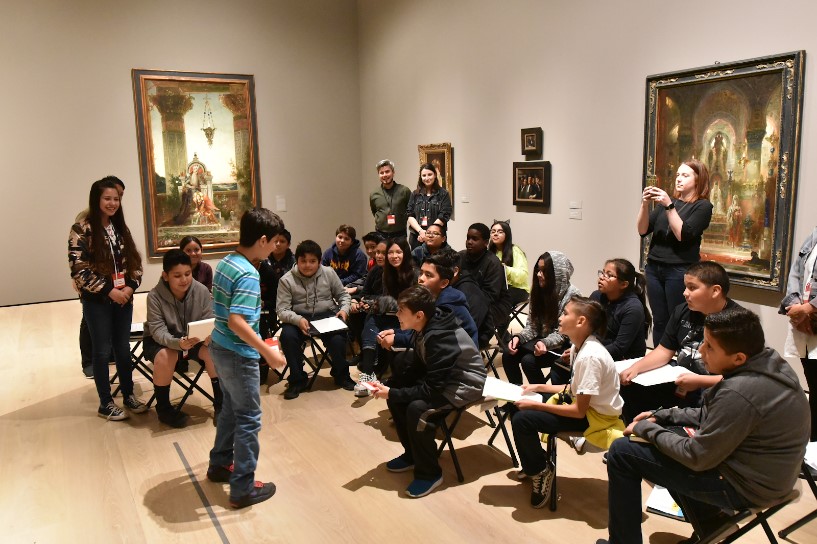 A young visitor stands in front of a larger group of visitors in a gallery. 