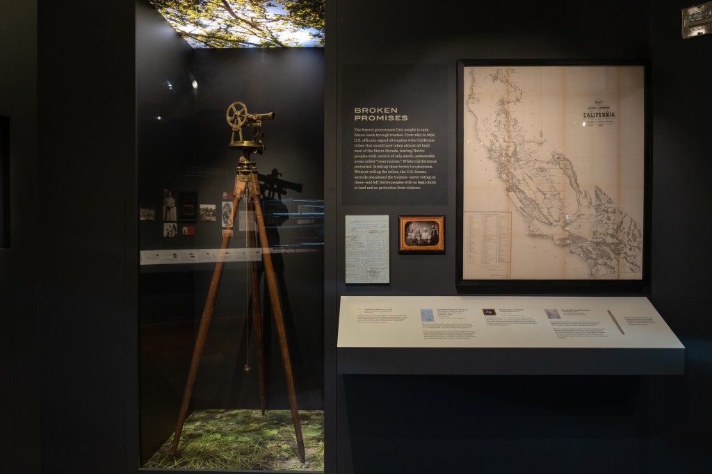 A view of the "Broken Promises" section, with a land-surveying tool, a map of the state of California, and several framed documents visible.