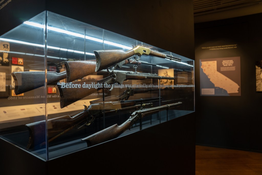 Guns are displayed in a clear case inscribed with quotes around the outside.