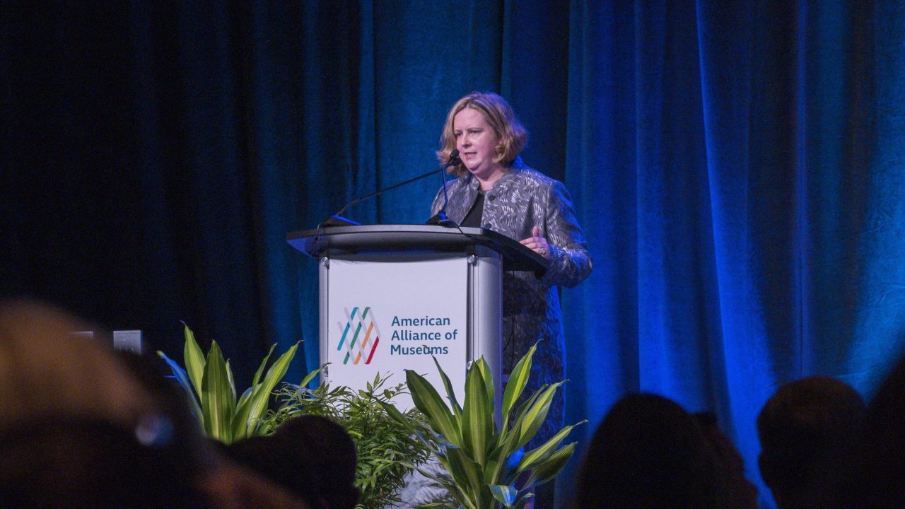 Laura Lott onstage at a podium with the AAM logo on it.
