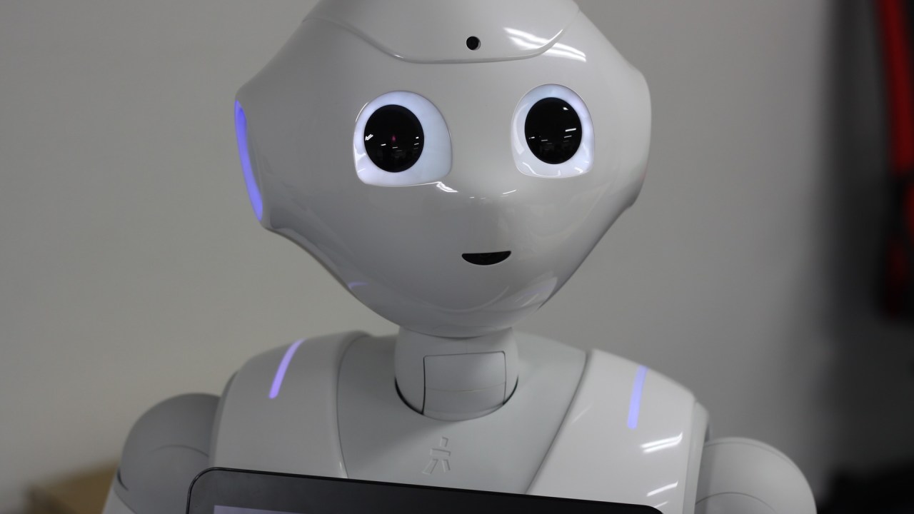 A plastic white robot with humanoid features and a touchscreen attached to its chest.