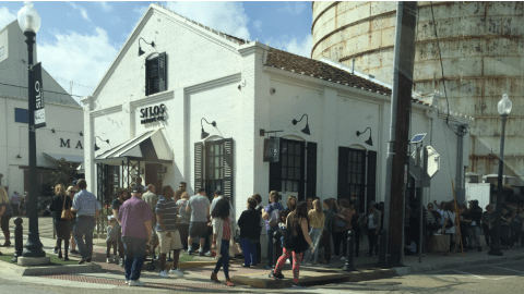 An exterior view of a building labeled "The Silos" in front of a grain silo, with a crowd of people lined up outside.