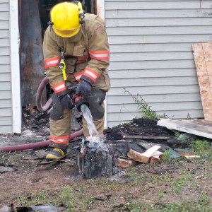 A firefighter is seen outdoors standing over a damaged artifact with a running hose.