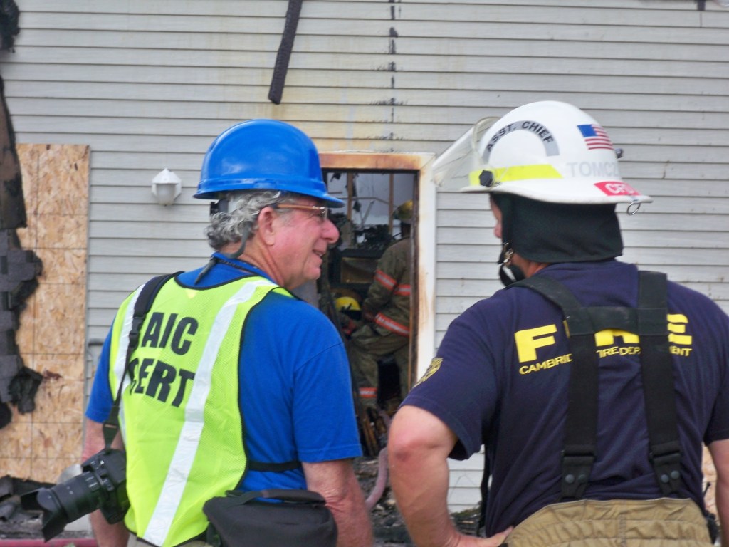 Herskovitz and Okerlund are seen outdoors in hard hats next to a fire-damaged building.