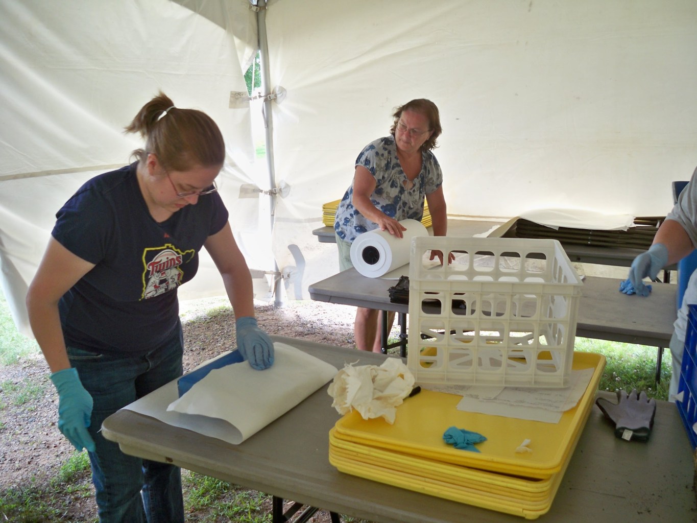 Two people are seen in a tent with wrapping artifacts in rolls of sheeting.