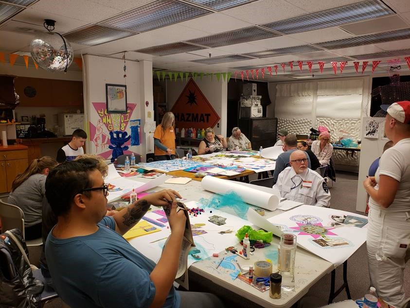 A group of people of mixed ages sits around a table with paper and various craft supplies.