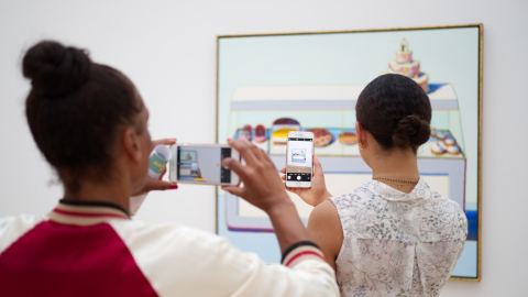 Two museum visitors hold take pictures of a Wayne Thiebaud painting on their smartphones.
