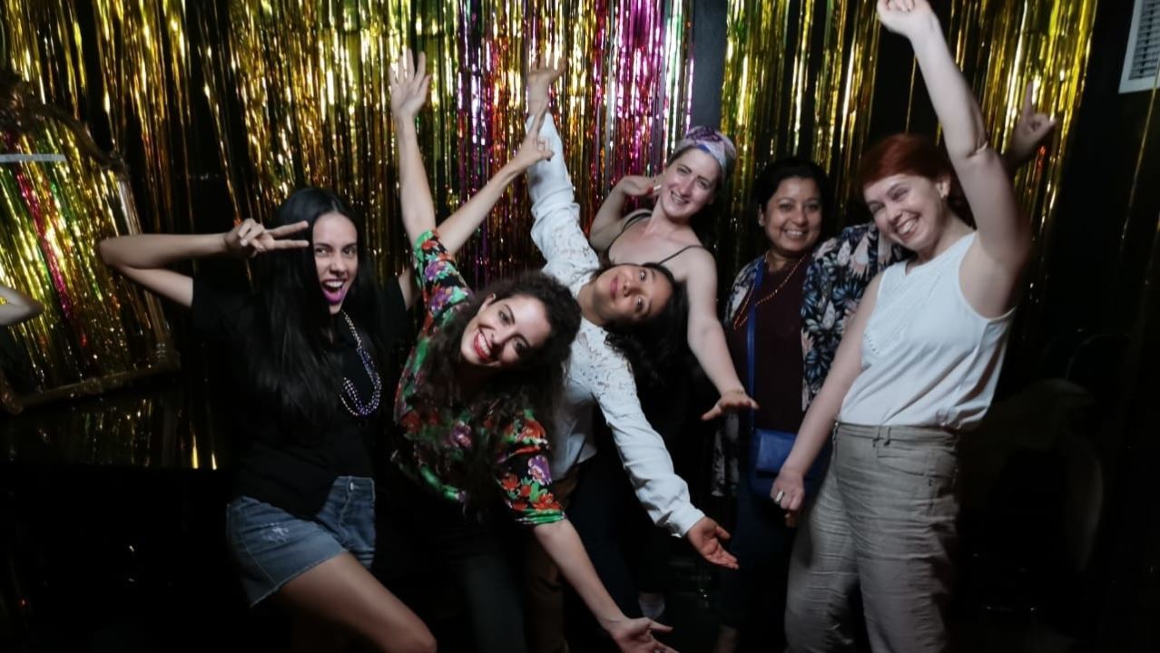 The participants pose with their arms up in front of a tinsel backdrop.