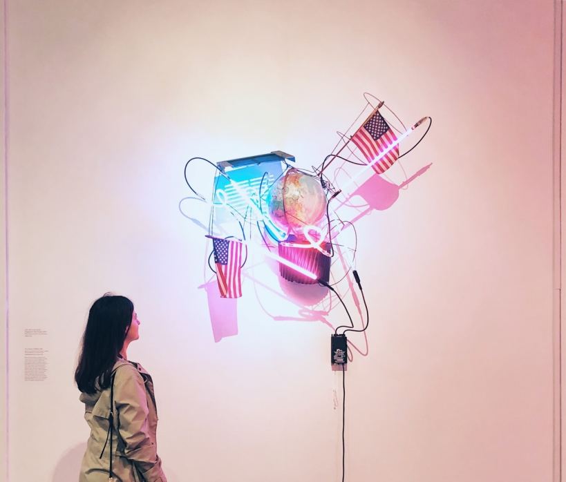 The author stands next to a sculpture made of neon tubes and handheld American flags, among other things.