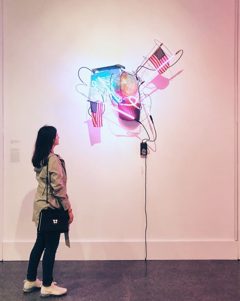 The author stands next to a sculpture made of neon tubes and handheld American flags, among other things.