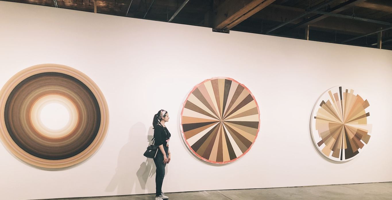 The author stands next to three circular canvases with geometric shapes in earth tones.