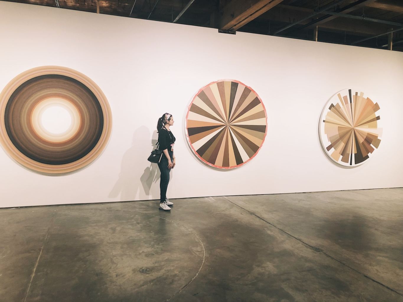 The author stands next to three circular canvases with geometric shapes in earth tones.