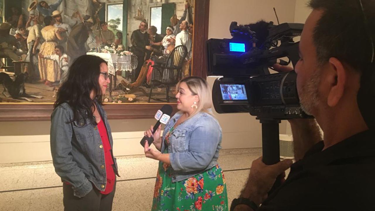 The author is seen standing in the museum talking to a reporter behind a camera.