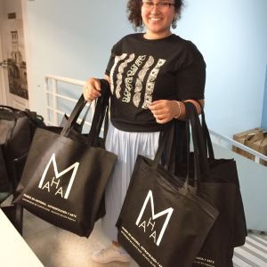 The intern stands with two armfuls of empty tote bags waiting to be filled.