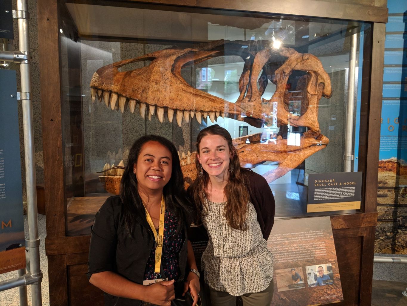 Tsiory and Susan pose together in front of a dinosaur fossil on display.