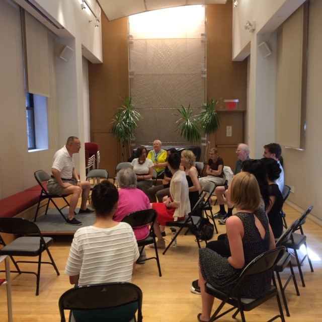 A group of people are seen gathered around someone seated on a small stage.