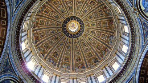 The interior view of a light-filled dome with intricately painted designs arcing up it in columns.