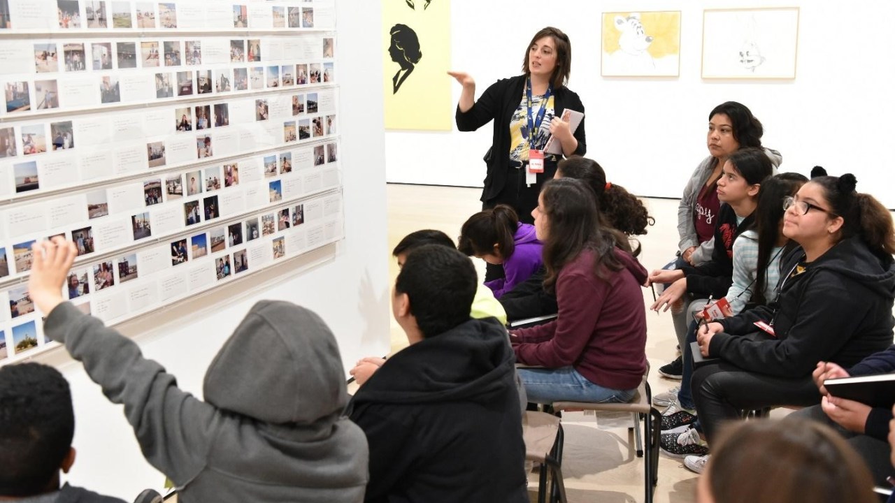 An instructor leads a group of children in a discussion of a work of art on display.