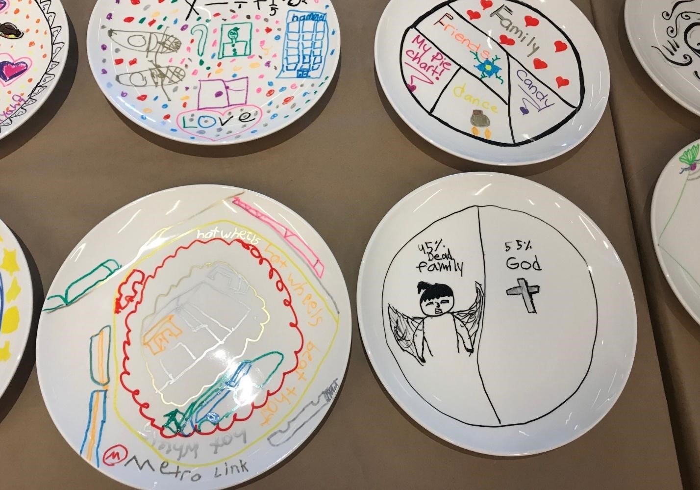 Among more colorful, elaborately designed plates, the grieving student's is shown: a simple black pie chart that says "45% dead family" and "55% God," with illustrations of an angel and a crucifix.