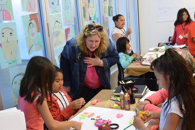 A teacher leans over a table where students work on an art project.