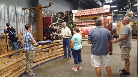 A group of participants stands around a display on the Spanish-American War