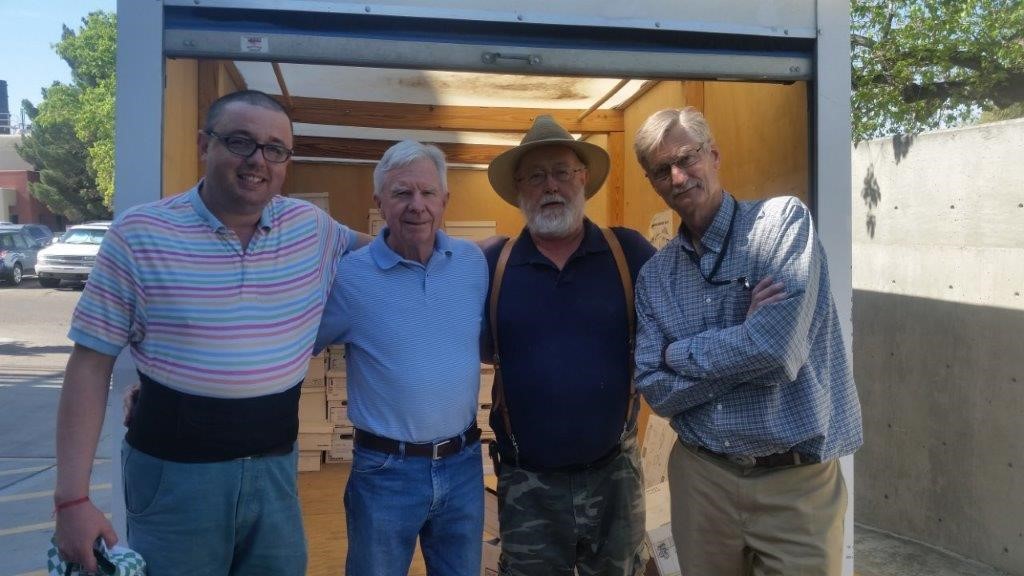 Four people pose on the street in front of the truck used to transport the collection, with the back hatch open to reveal the boxes containing the objects.
