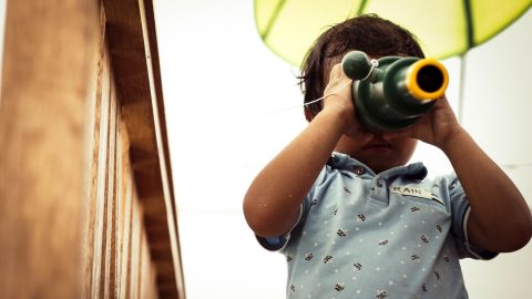 A young child looks through binoculars.