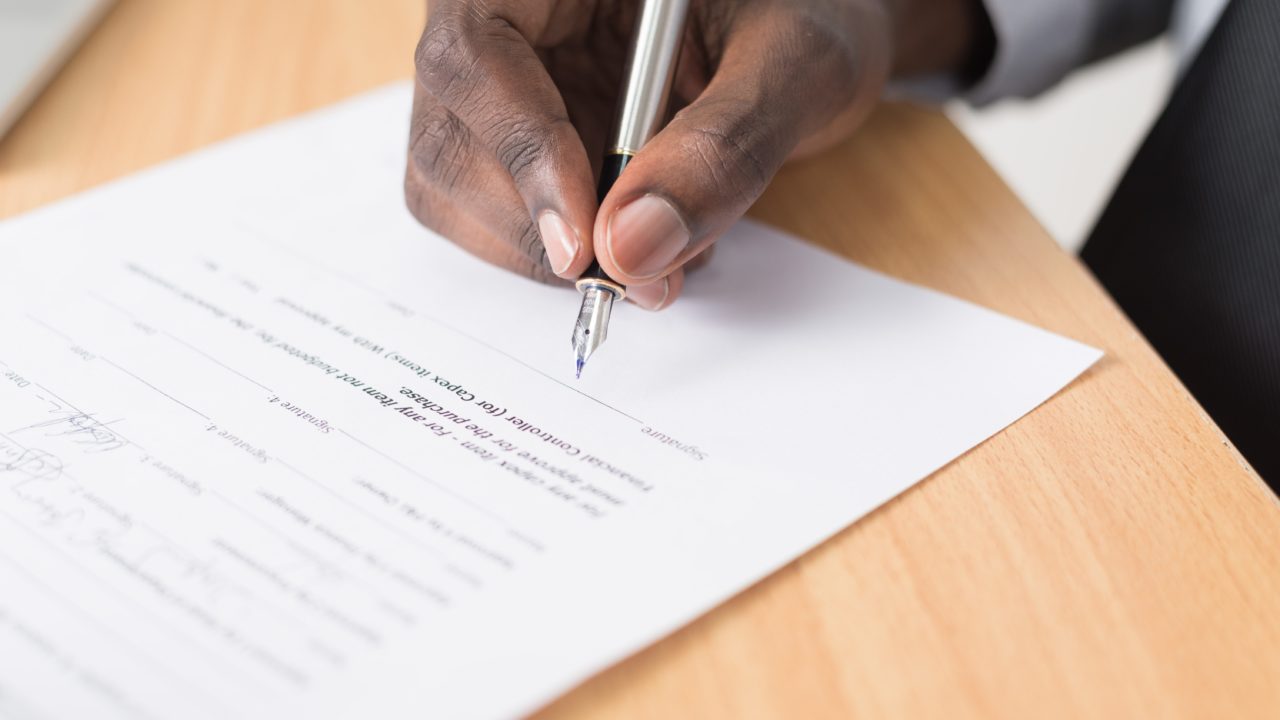 A person holding a pen to sign a contract.
