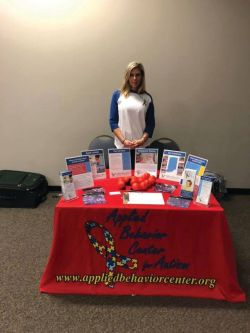 A woman stands behind a table with various pamphlets on top.