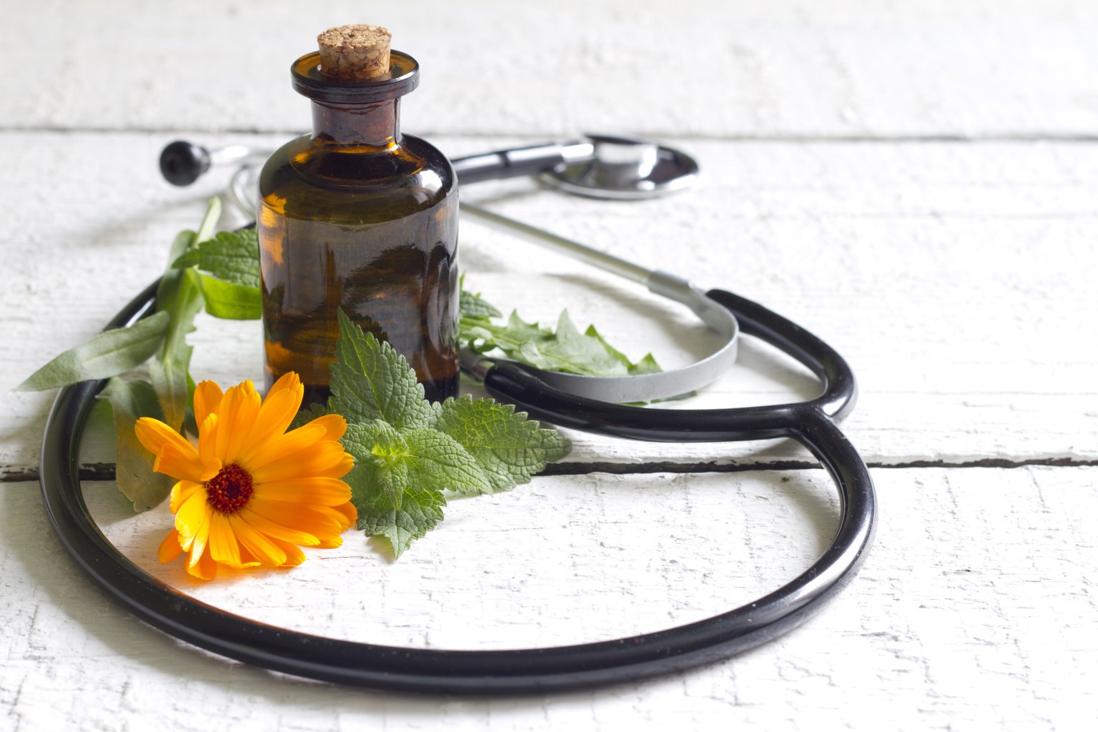 A stethoscope laying on a wooden table with a flower and brown glass jar. 