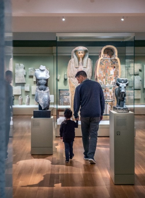 An adult and child tour a gallery of Ancient Egyptian artifacts.