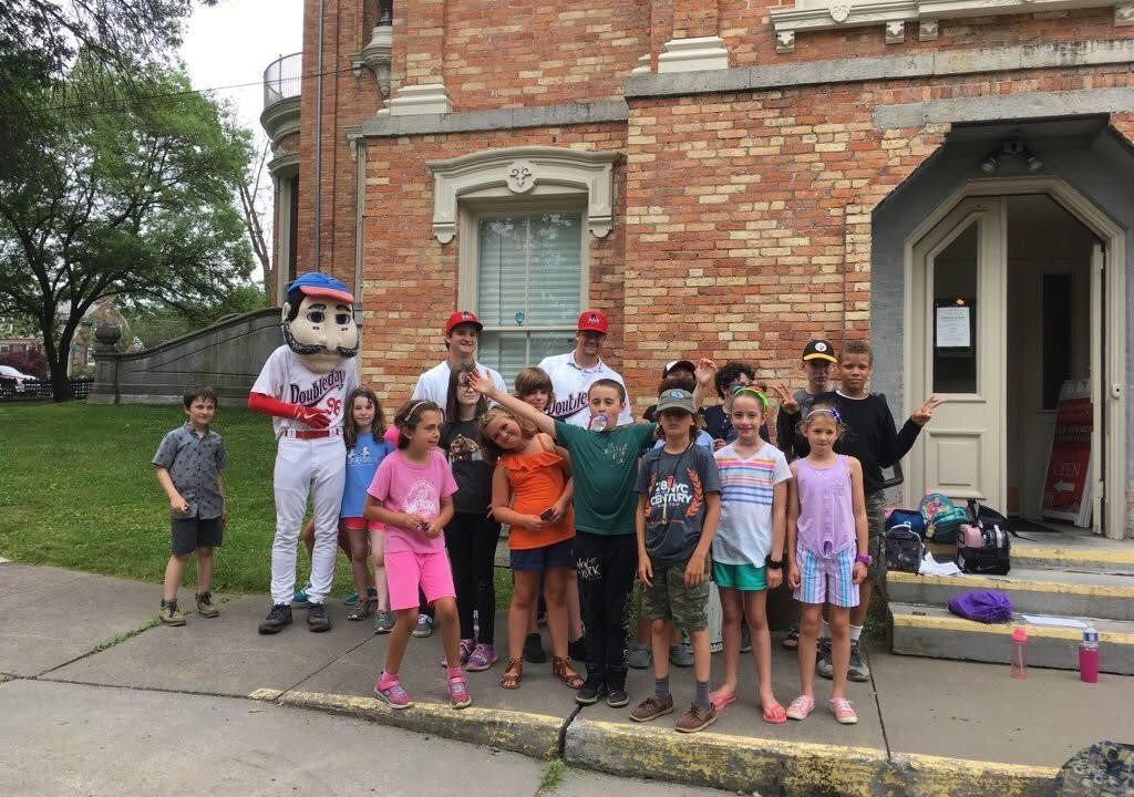 Campers pose for a group portrait in front of a museum with someone in an Abner Doubleday costume.