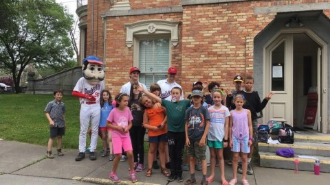 Campers pose for a group portrait in front of a museum with someone in an Abner Doubleday costume.