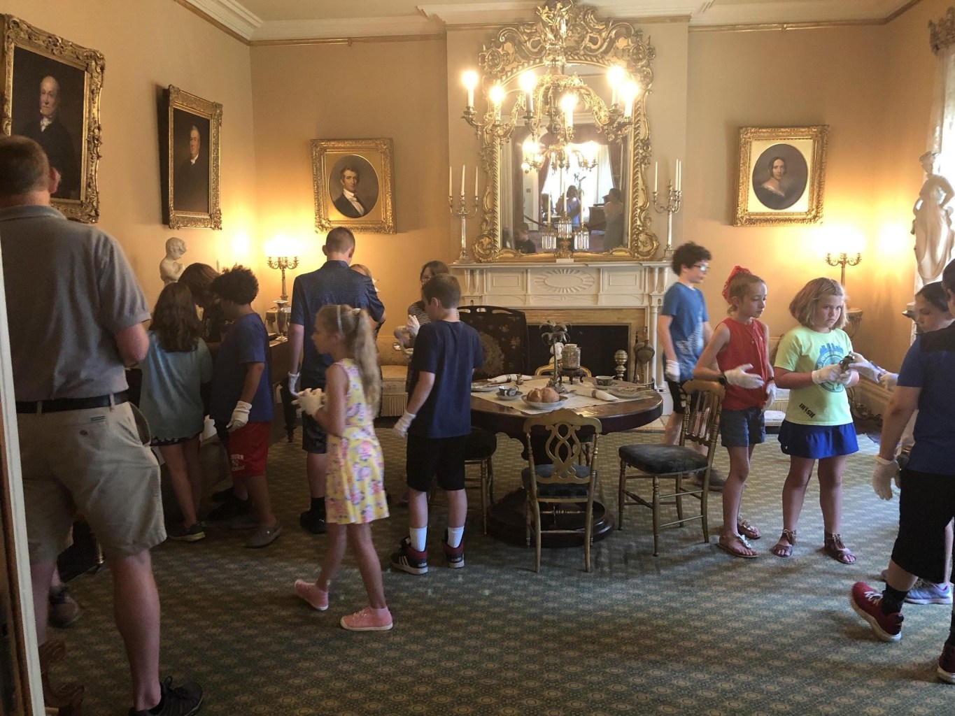 A group of campers wearing white gloves explore the interior of a historic house.