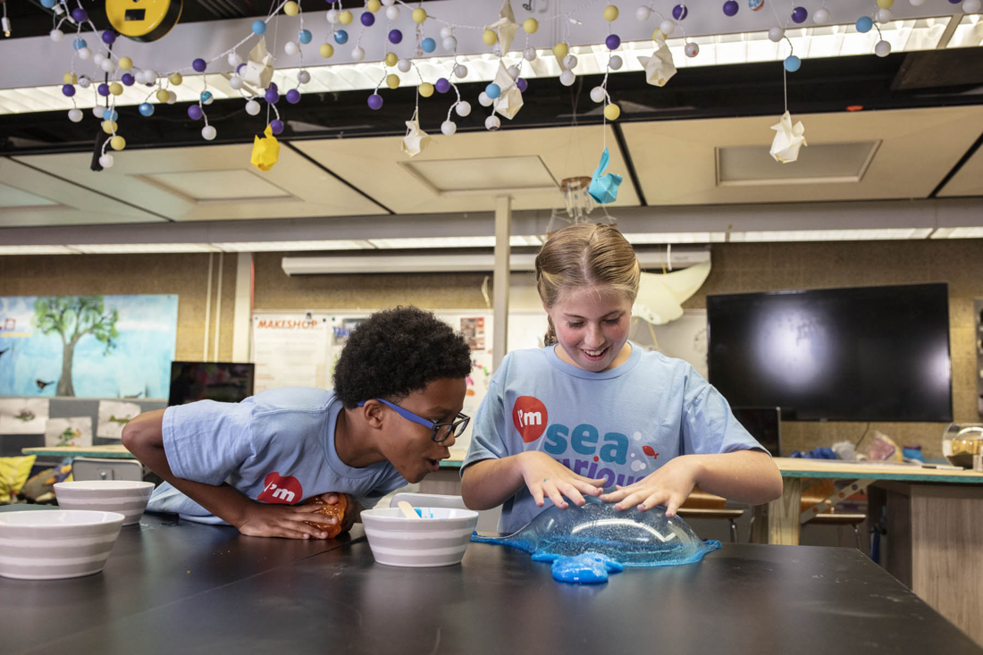 Two kids in a science classroom setting play with slime.