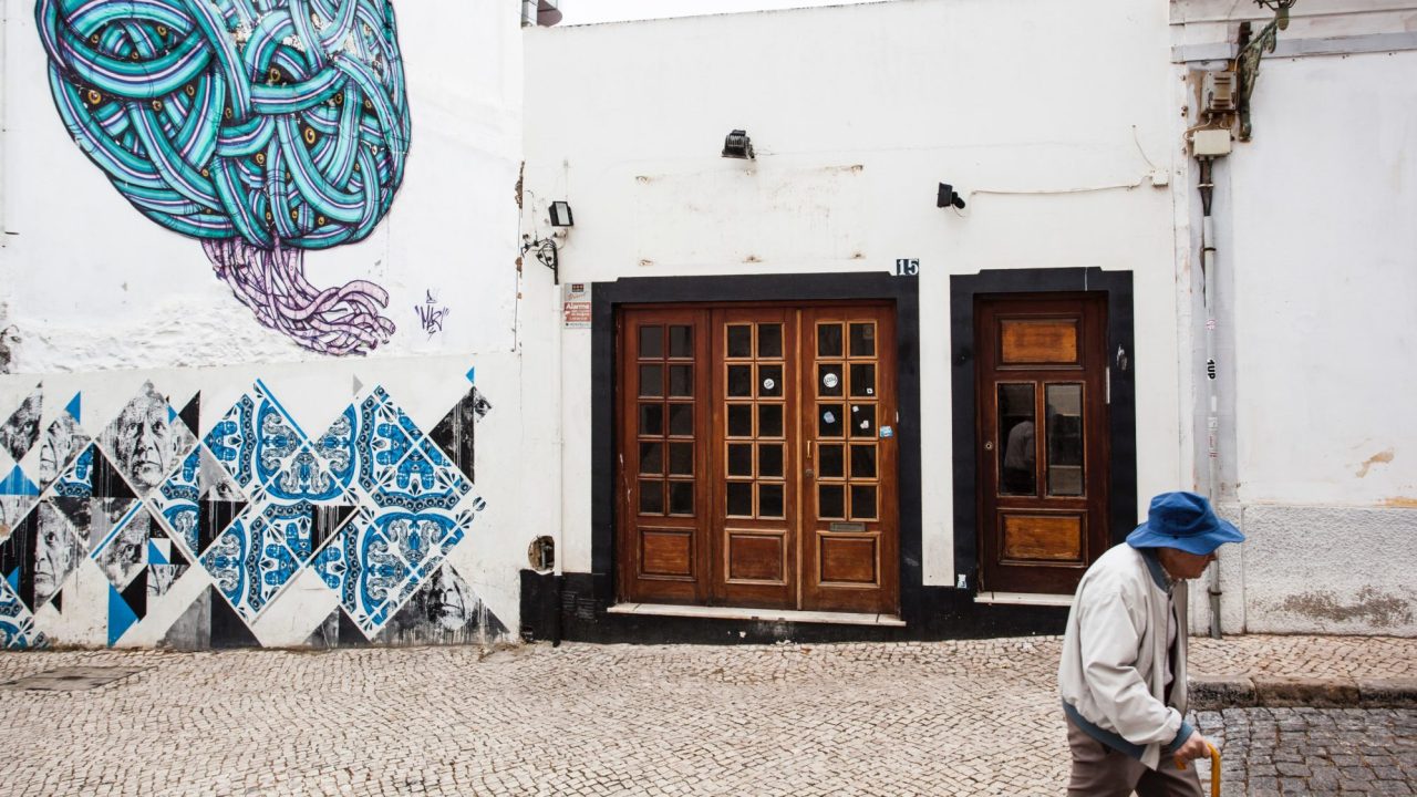 An older person walks past a building decorated with street art.