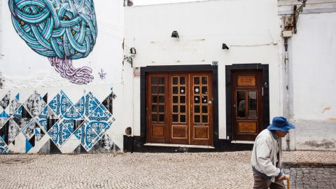 An older person walks past a building decorated with street art.