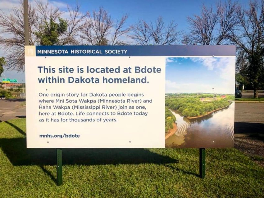 An outdoor sign that reads "This site is located at Bdote within Dakota homeland. One origin story for Dakota people begins where Mni Sota Wakpa (Minnesota River) and Haha Wakpa (Mississippi River) join as one, here at Bdote. Life connects to Bdote today as it has for thousands of years.