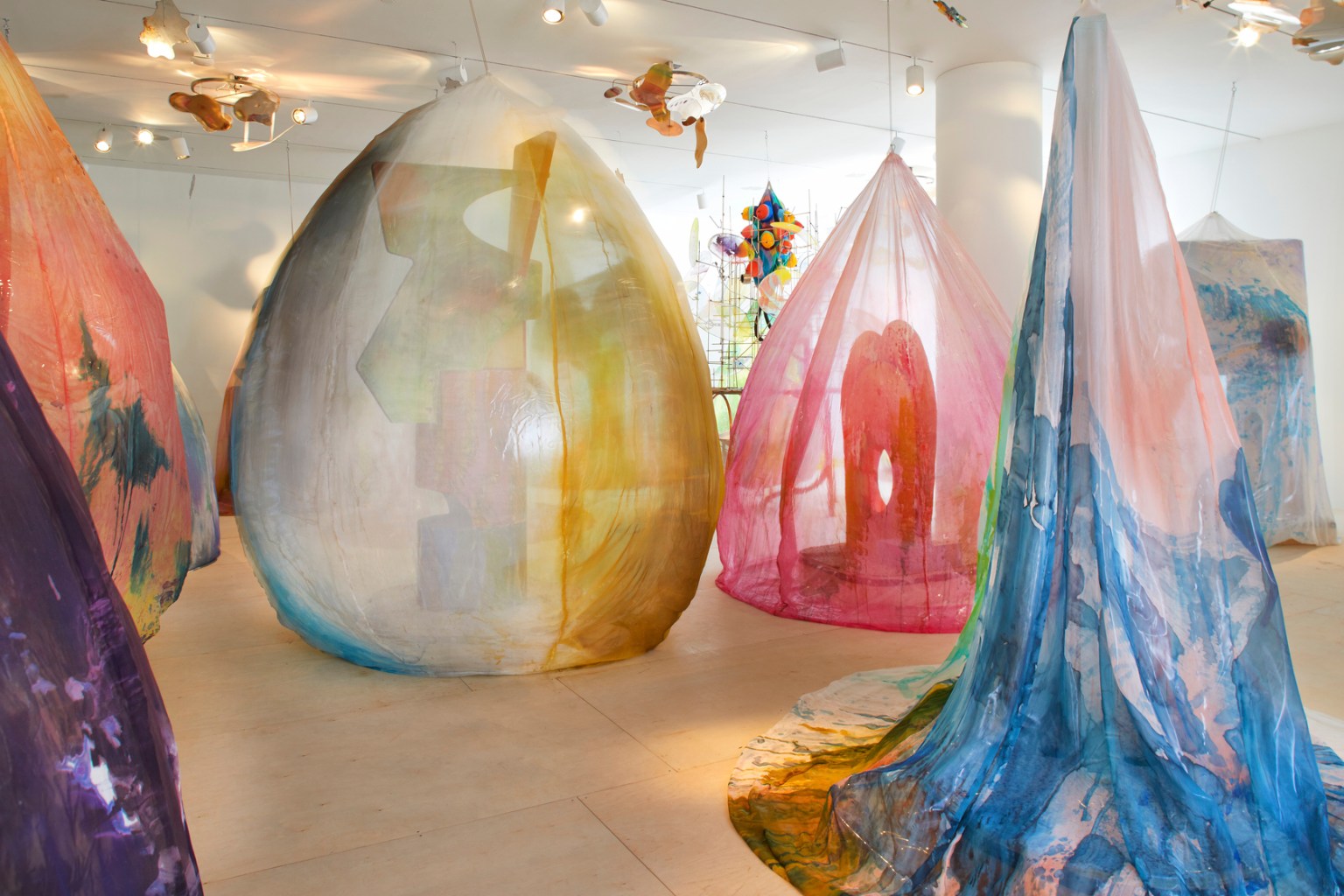 Abstract sculptures are draped in transparent textiles dyed with patterns of bright color.