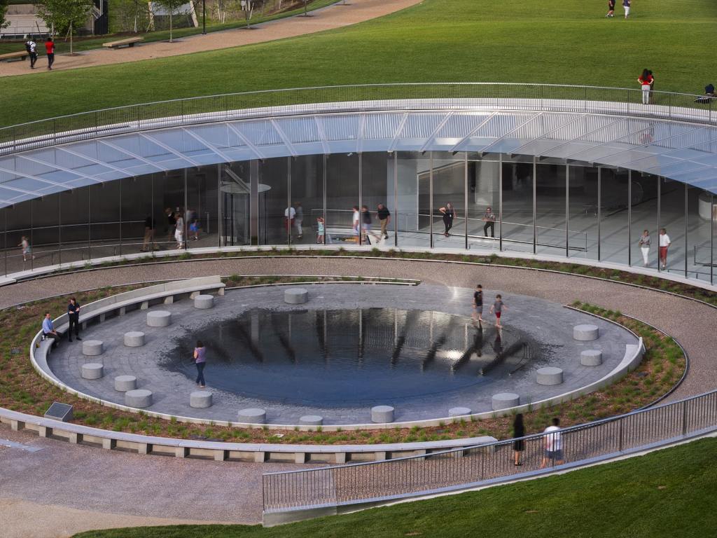 A close-up of the entry to the Gateway Arch Museum, with sloped pathways instead of stairs and a small reflecting pool with benches and chairs around it.