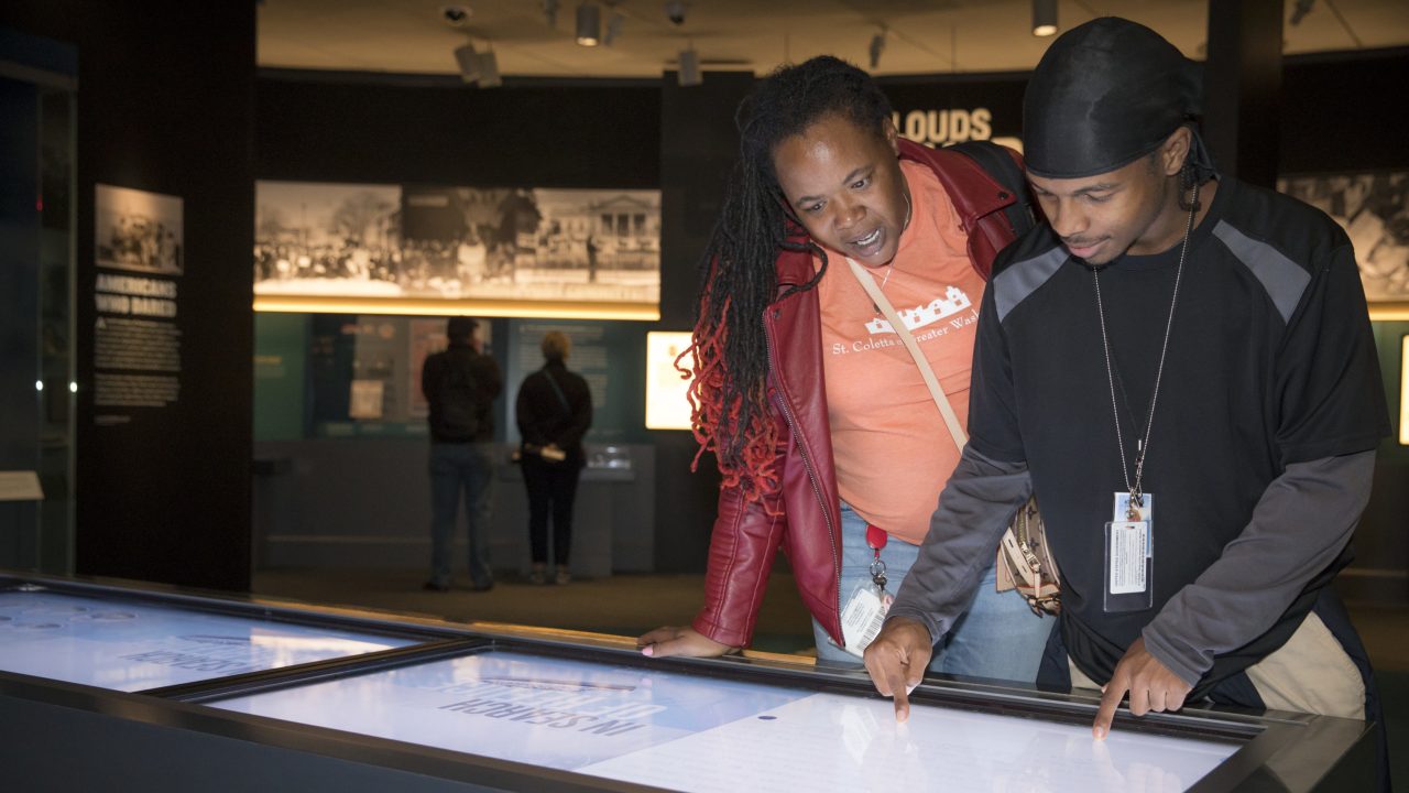 Two people bent over an interactive display table in a museum gallery.