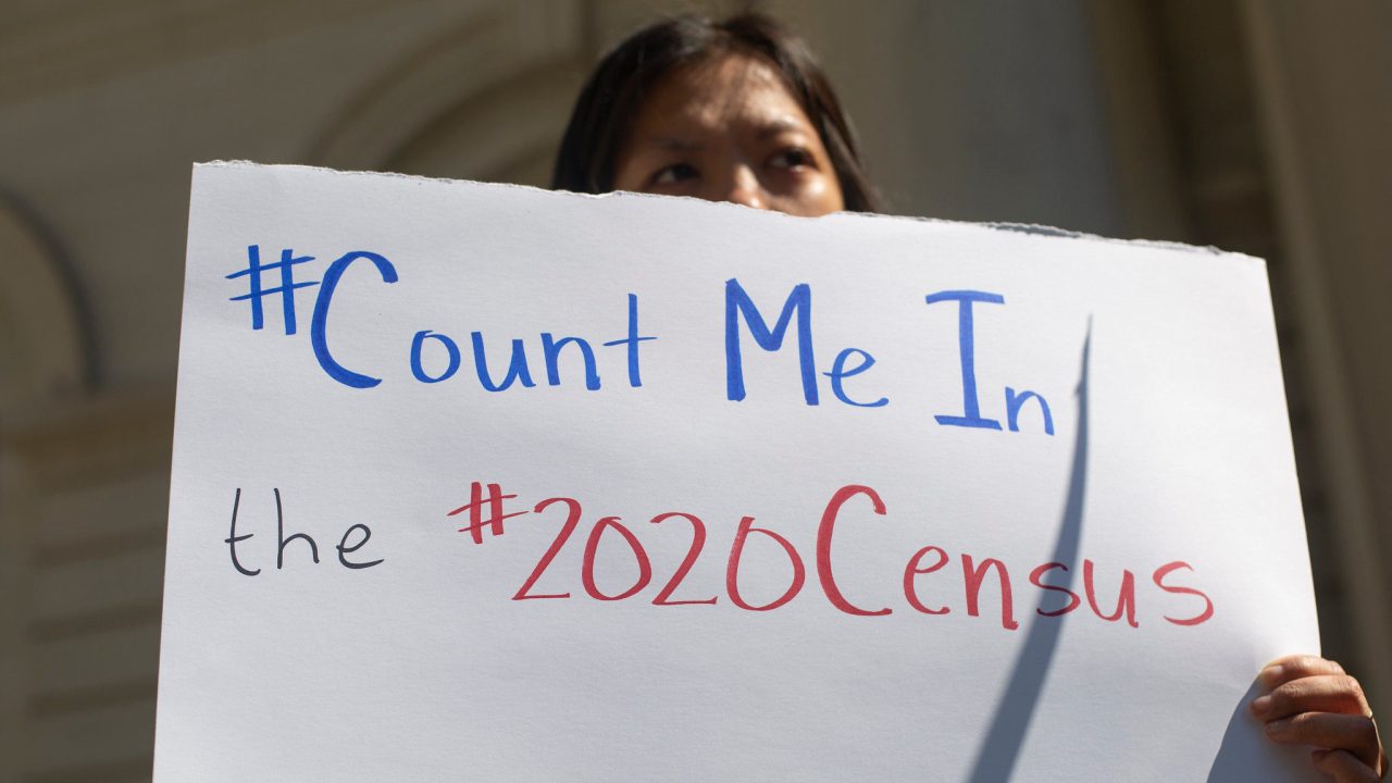 A protester behind a sign that says "#Count Me In the #2020Census. #lovetransforms."