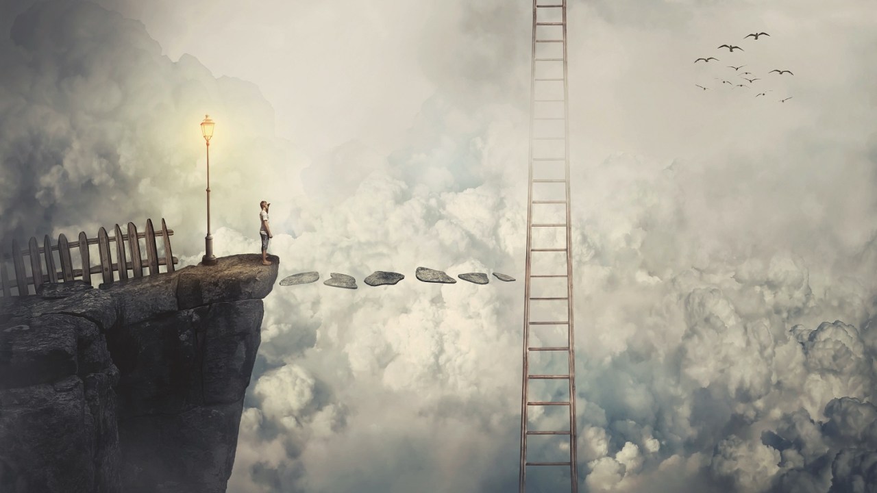A person stands on a precipice looking out into an abyss of clouds with a single ladder leading toward the sky about halfway across the chasm.