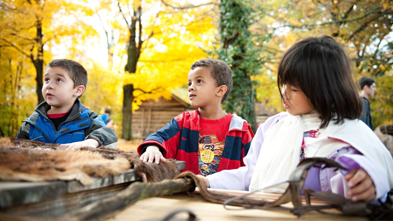 Three children standing outside touching fur pelts