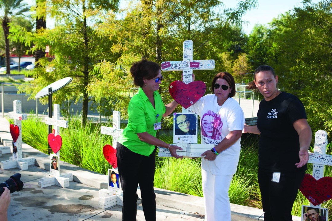 Two women stand beside the Pulse night club holding a cross and pictures. 